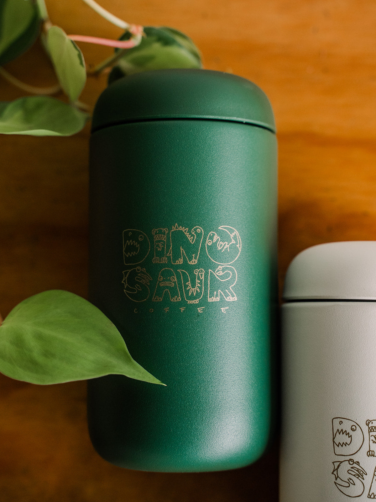 A close up of a green tumbler that reads "dinosaur coffee" in gold animal-shaped lettering